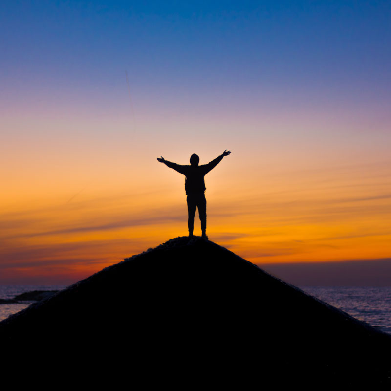 Person with pandemic travel insurance triumphantly reaches a summit at sunset.